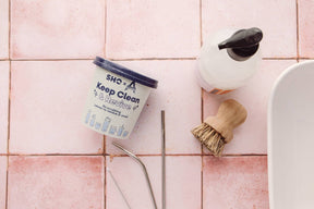 SHO clean and revive powder on a pink tiled surface with straws, soap and brushes