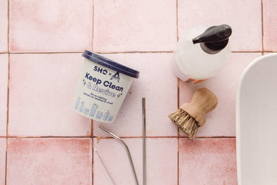 SHO clean and revive powder on a pink tiled surface with straws, soap and brushes